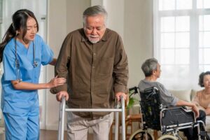 A caregiver helping an older adult use hand sanitizer in a bright, communal living area.