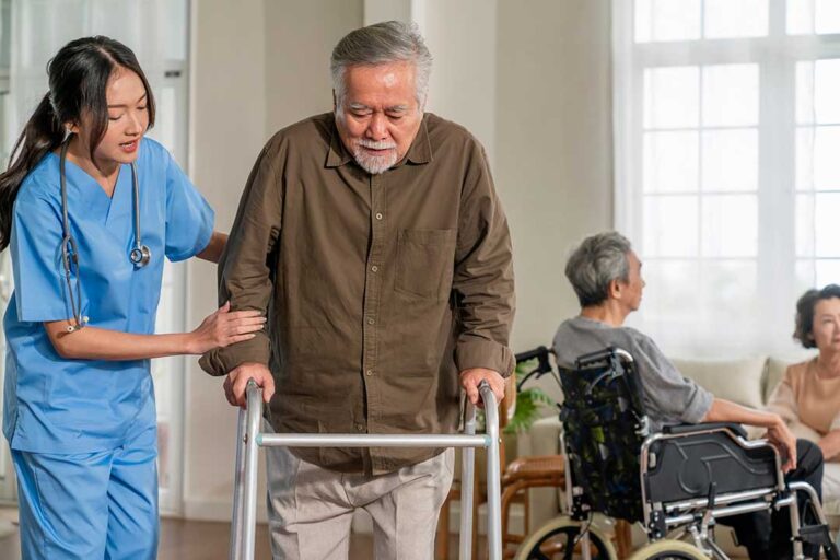 A caregiver helping an older adult use hand sanitizer in a bright, communal living area.